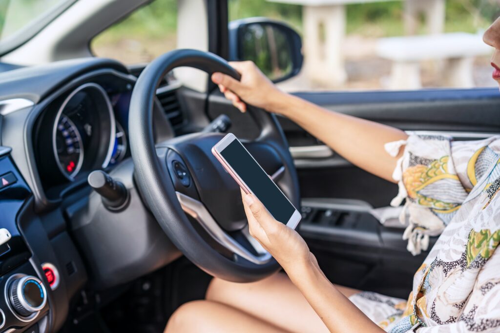 Young female driver using a phone while driving, indicating negligence. Driver negligence compensation.